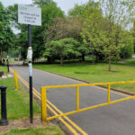 A yellow barrier across an accesss road to Nuneaton's Registry Office. To the left of the barrier are two black bollards. There is a pavement to the left of the road, and a grass buffer between the two. Next to the barrier is a sign that reads "Barrier will be closed at 5pm".